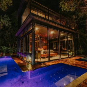Experience a night in a luxury secluded glass house with a glowing pool surrounded by jungle.