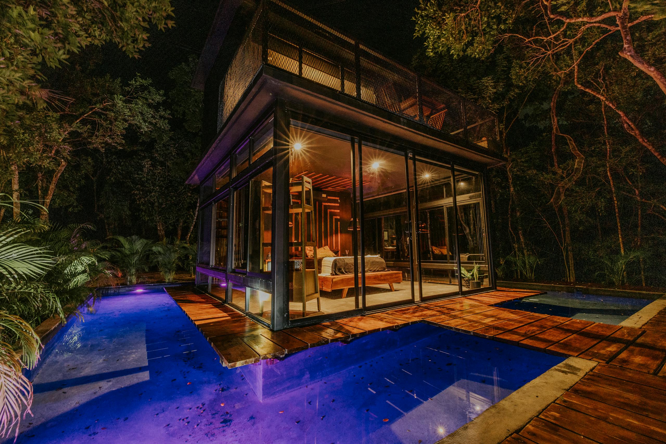 Experience a night in a luxury secluded glass house with a glowing pool surrounded by jungle.